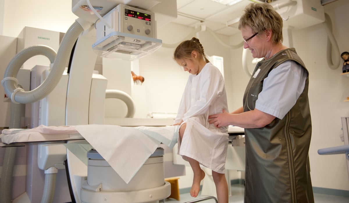 Ung flicka sitter vid en röntgenmaskin bredvid en sjukvårdspersonal