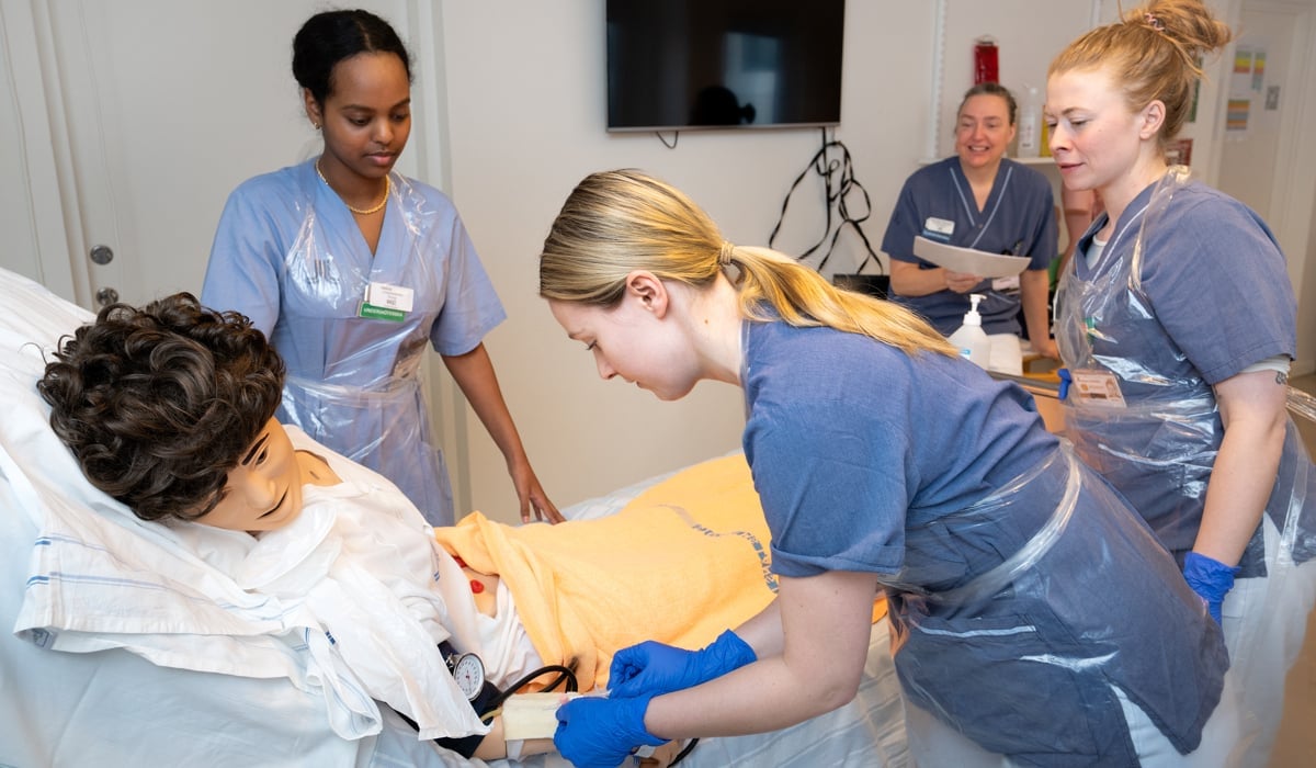 Bild på fyra personer i sjukhuskläder som övar på en docka