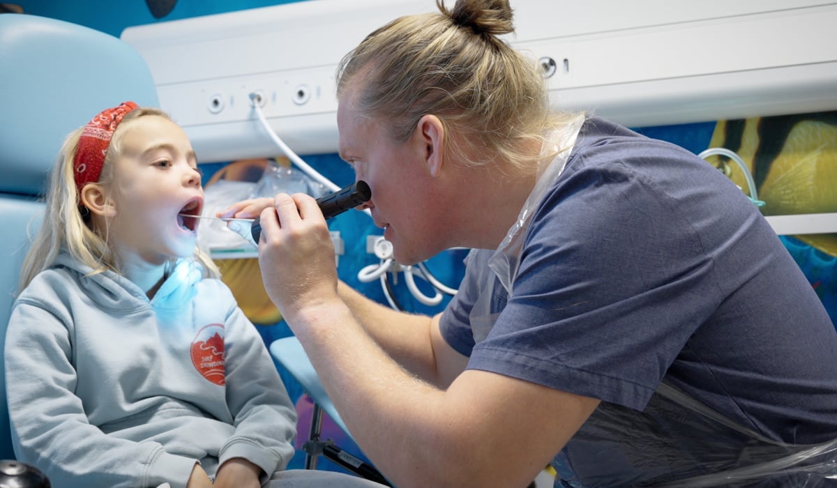 manlig läkare lyser flicka i munnen.