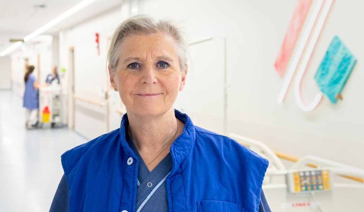 Kvinna klädd i blå vårdkläder tittar in i kameran