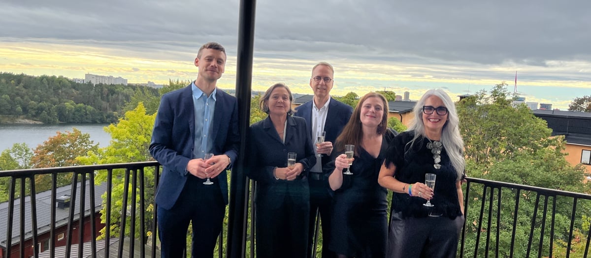 gruppbild 5 festklädda personer med glas i händerna står på balkong